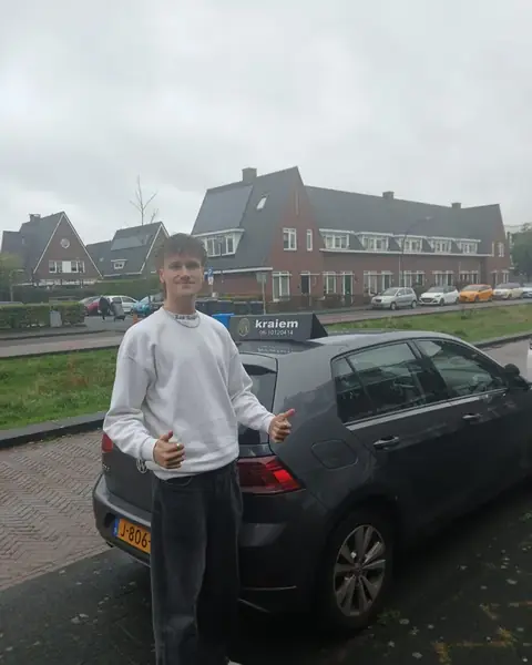 Geslaagde leerling met duimen omhoog naast de lesauto van Rijschool Kraiem in Tilburg