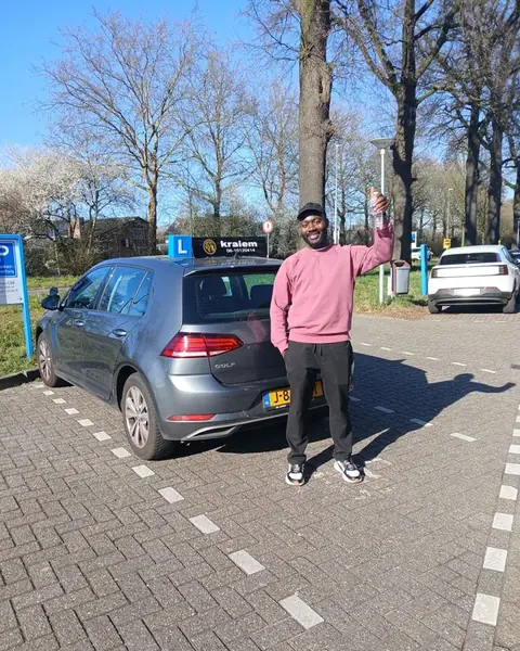 Geslaagde leerling houdt zijn rijbewijs omhoog naast de lesauto van Rijschool Kraiem